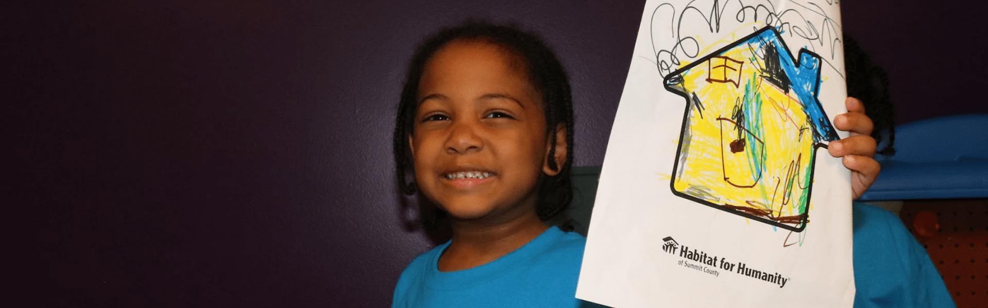 Child smiling holding up hand drawn picture of future home