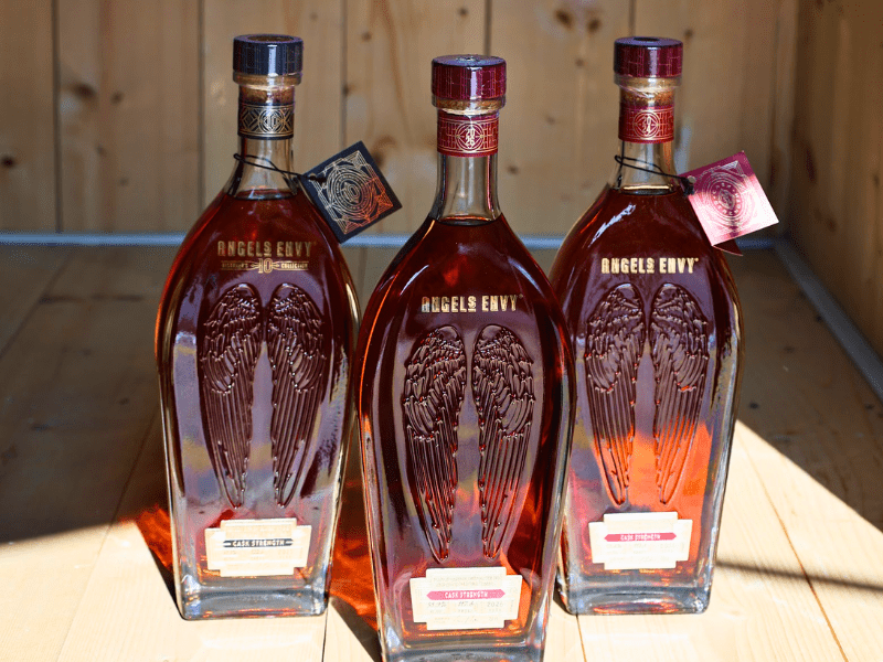 Three bottles of Angel's Envy Cask Strength bourbon standing side-by-side on a wooden surface for the Welcome Home Social raffle.