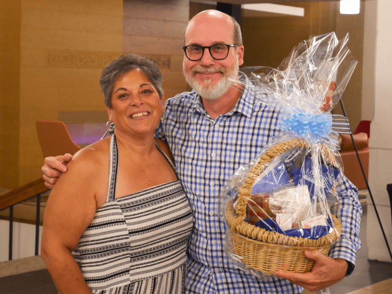 Habitat for Humanity President and CEO Rochelle posing with last year's Welcome Home Social raffle winner, who is smiling and holding a large wrapped gift basket.